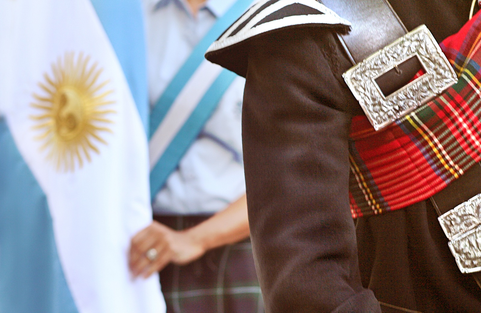 Person wearing tartan standing beside another person holding the flag of Argentina