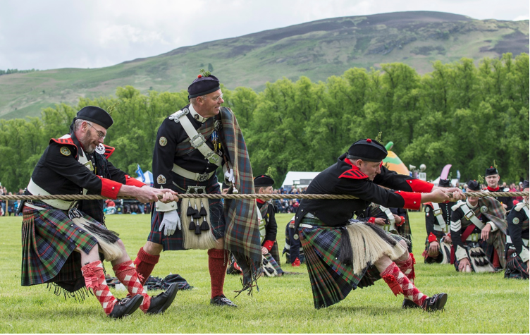 Three men playing tug of war at the highland games, in traditional highland dress, sash, kilts, socks.