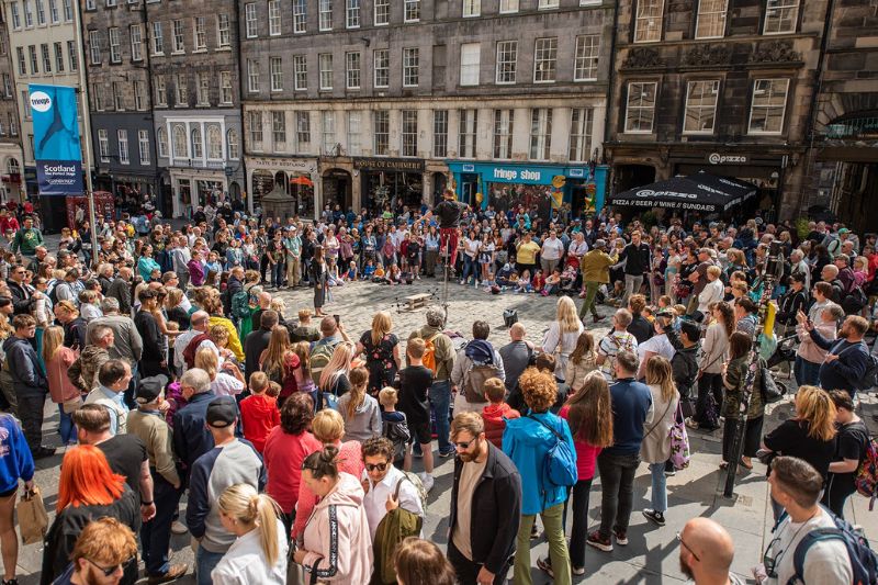 Artist performing an act at the Edinburgh Fringe Festival surrounded by a large crowd